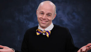 Matt Townsley holding both hands palms up with a smile, wearing a purple and gold bow tie.